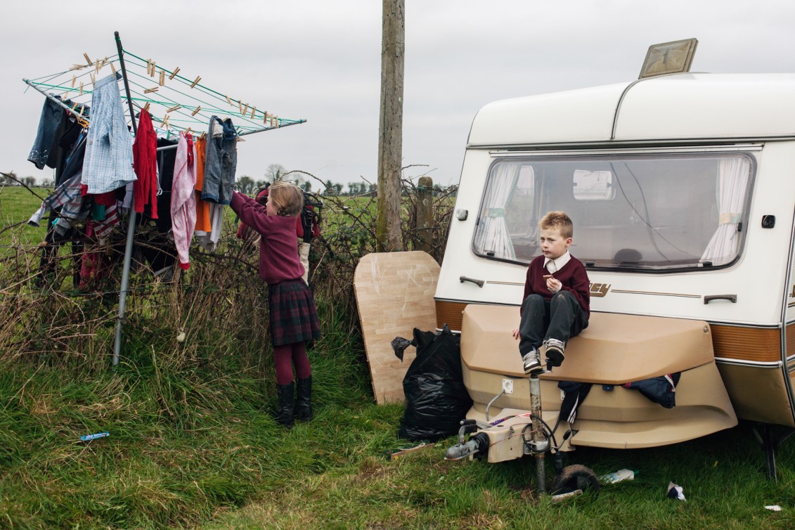 James is sitting on a campingbox while her sister is hanging up the clothers after coming back from school at the backroad, County Kildare, Ireland